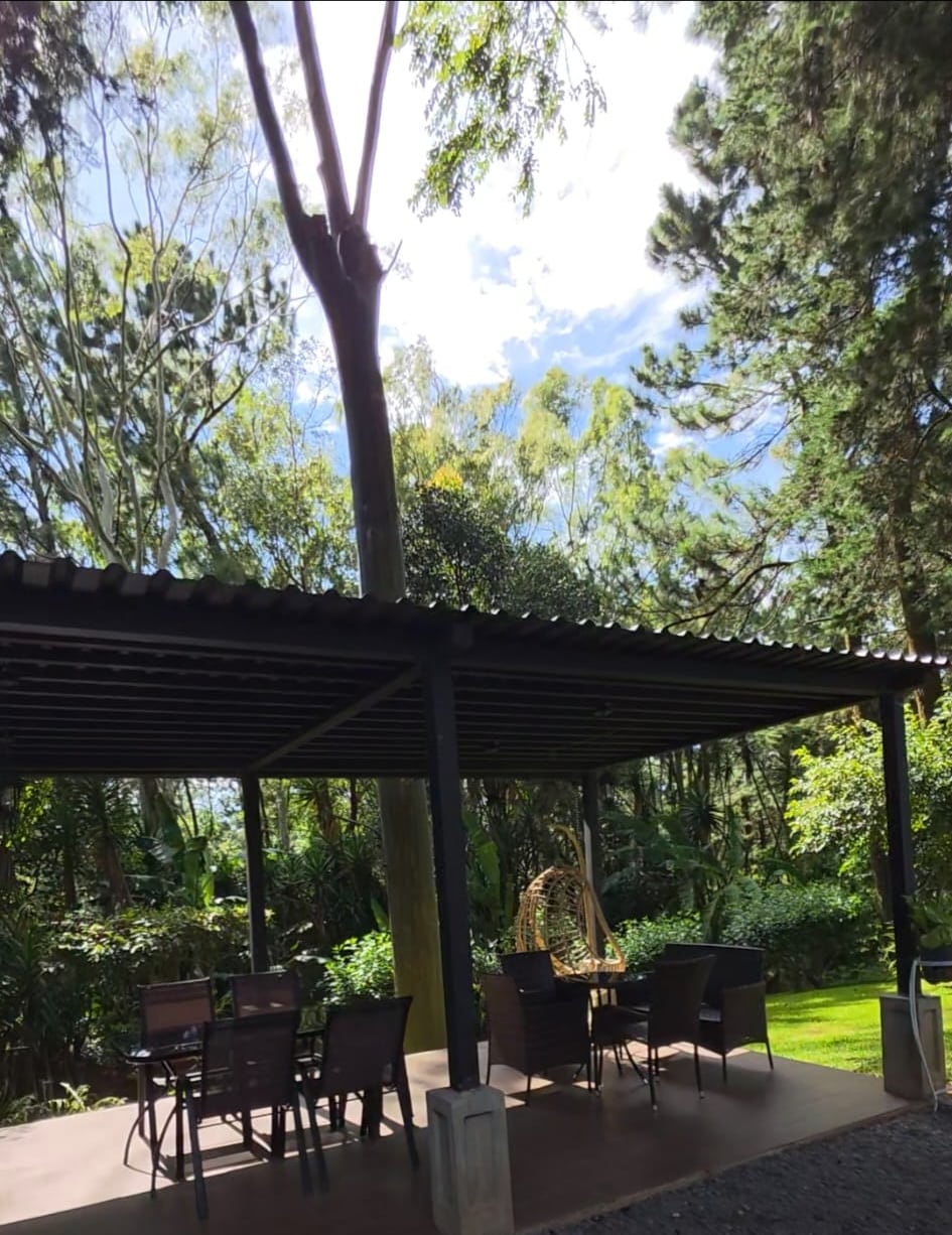 The large covered terrace of the colonial house, with two seating areas and a hanging chair under the pines
