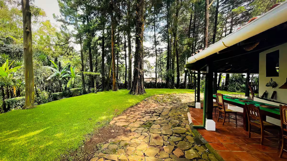 The tiled veranda of the colonial house with its long table, opening onto the lawn and pine forest